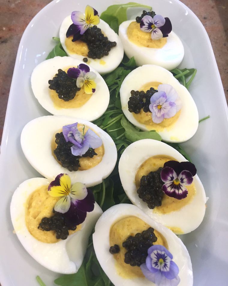 Devilled eggs topped with caviar and pansies on rocket