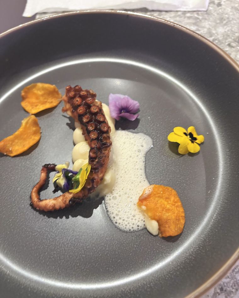 Octopus with sweet potato crisps and a light sea foam on a grey plate
