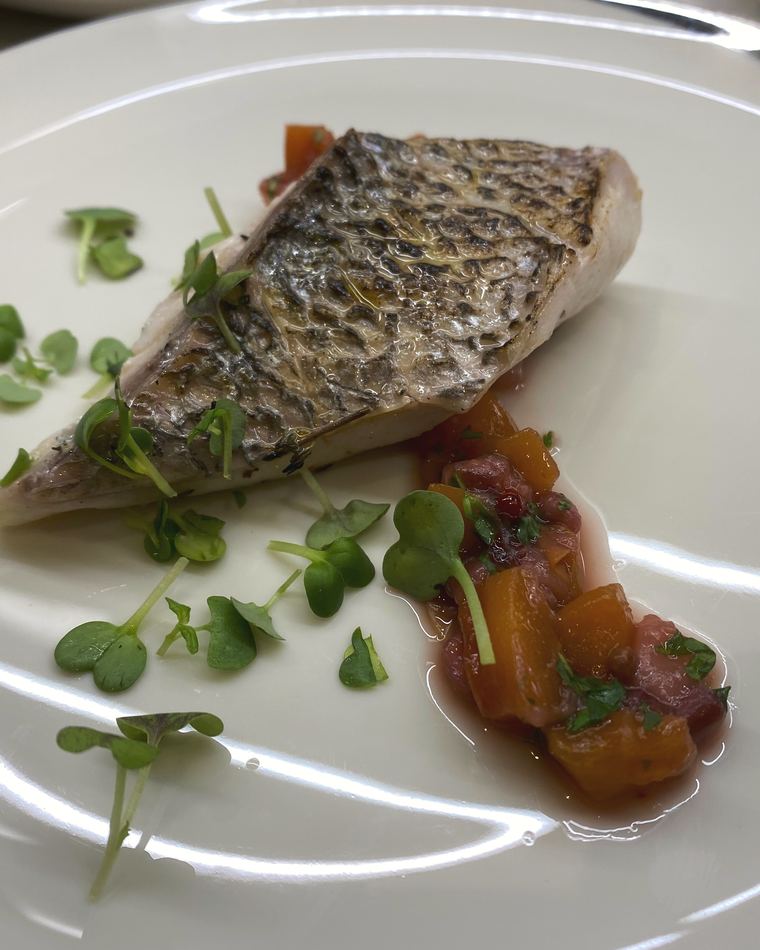 Sea bass with confit tomato and micro herbs on a white plate