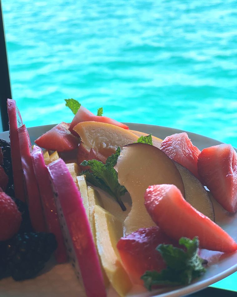 A fruit plate held above turquoise water