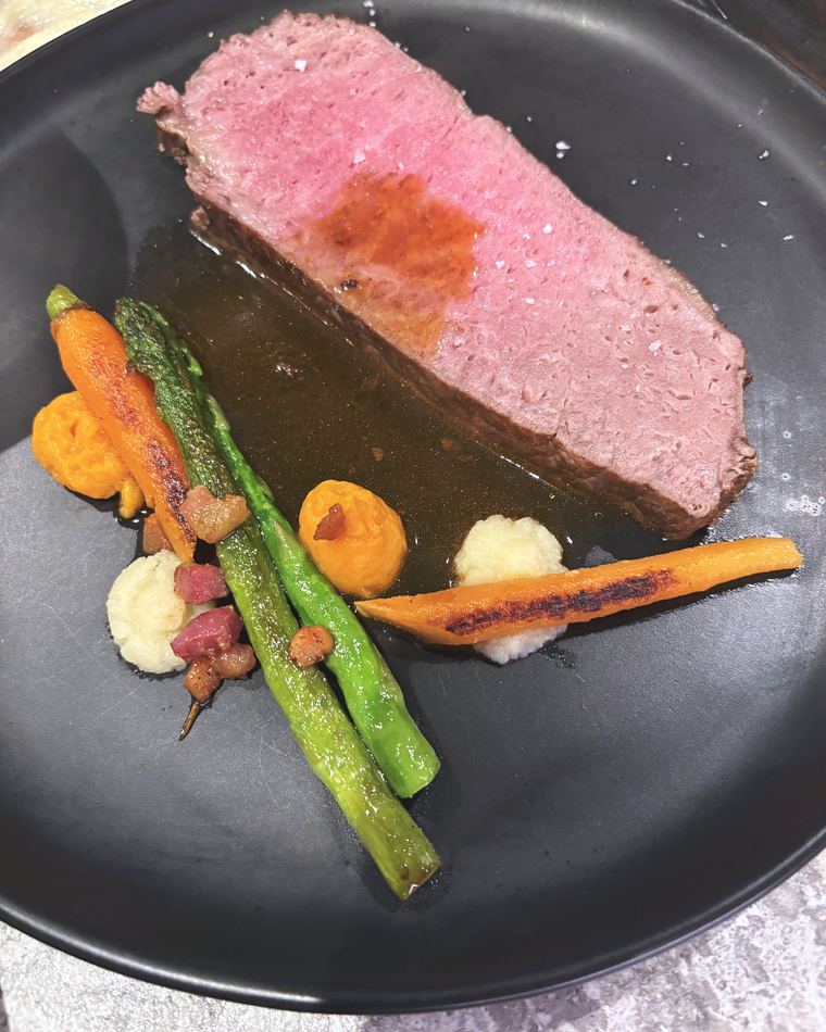 Sliced rare beef with asparagus and baby carrots on a dark plate