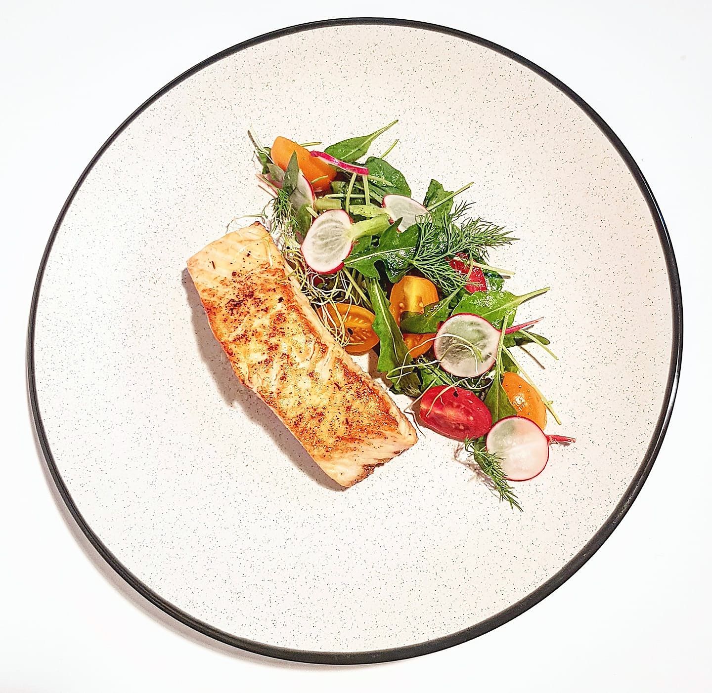 Seared salmon with heirloom tomato and micro-herb salad on a speckled plate